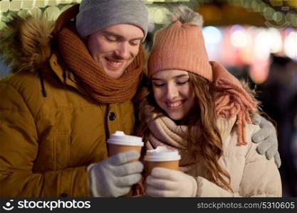 winter holidays, hot drinks and people concept - happy young couple with coffee over christmas lights in evening. happy couple with coffee over christmas lights