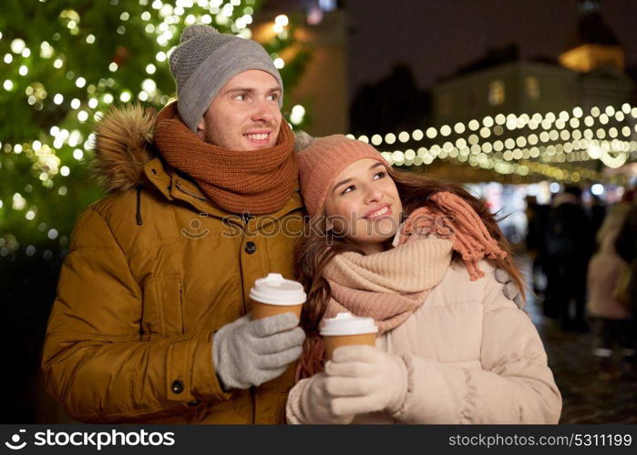 winter holidays, hot drinks and people concept - happy young couple with coffee at christmas market in evening. happy young couple with coffee at christmas market