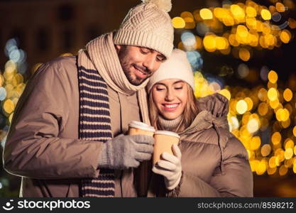 winter holidays, hot drinks and people concept - happy young couple with takeaway coffee cups in christmas city in evening. happy young couple with coffee in christmas city