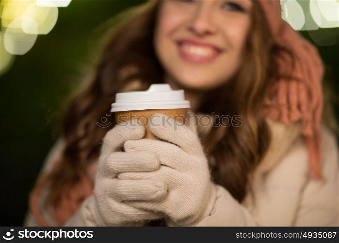 winter holidays, hot drinks and people concept - happy young woman with coffee over christmas lights outdoors. happy woman with coffee over christmas lights