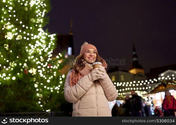 winter holidays, hot drinks and people concept - happy young woman with coffee at christmas market in evening. happy young woman with coffee at christmas market