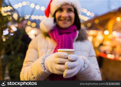 winter holidays, hot drinks and people concept - happy young woman with coffee or mulled wine in cup at christmas market in evening. woman with cup of hot drink at christmas market