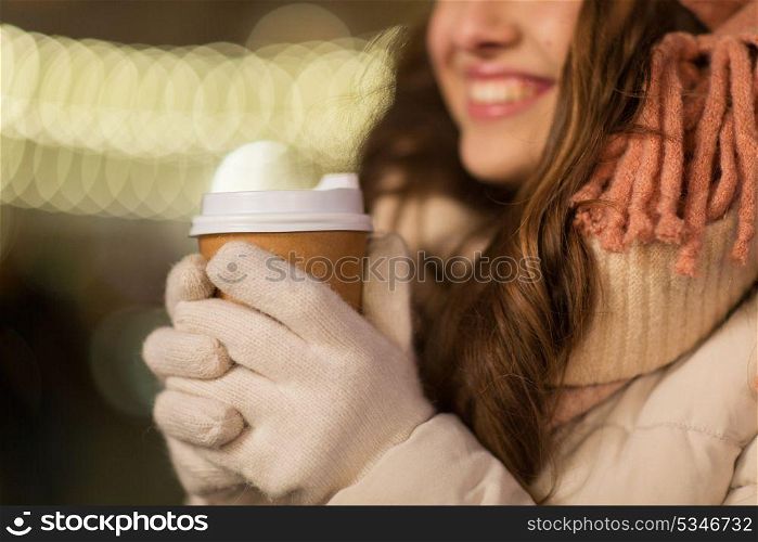 winter holidays, hot drinks and people concept - happy young woman with coffee over christmas lights outdoors. happy woman with coffee over christmas lights