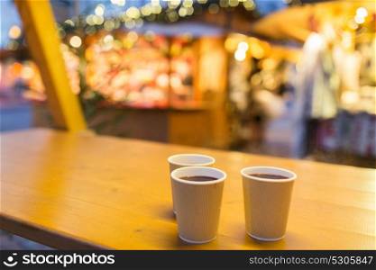winter holidays, hot drinks and people concept - mulled wine in disposable paper cups on table at christmas market. mulled wine in paper cups at christmas market