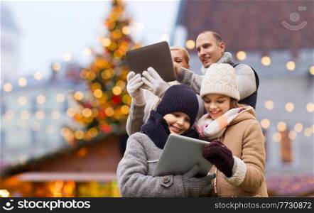 winter holidays, leisure and people concept - happy family with tablet pc computers over christmas market background. happy family with tablet pc at christmas market