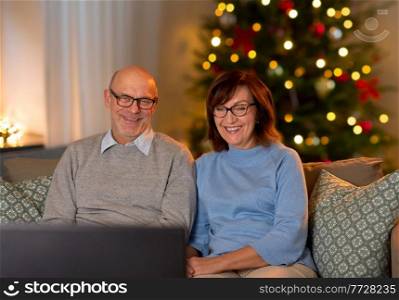 winter holidays, leisure and people concept - happy smiling senior couple watching tv at home in evening over christmas tree lights on background. happy senior couple watching tv on christmas
