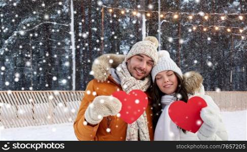 winter holidays, love and christmas concept - happy couple holding blank red hearts over ice skating rink background. happy couple with red hearts at ice rink in winter