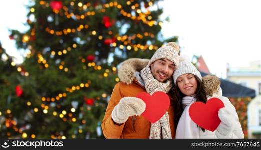 winter holidays, love and people concept - happy couple holding blank red hearts over christmas market background. happy couple with red hearts at christmas market