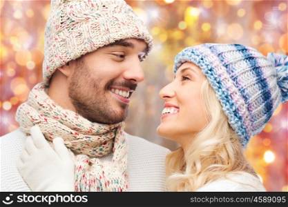 winter, holidays, love, christmas and people concept - close up of smiling man and woman in hats and scarf over lights background