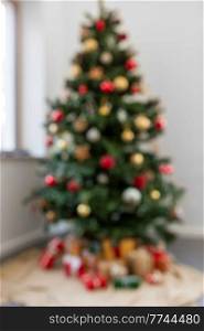 winter holidays, new year and celebration concept - blurred decorated green artificial christmas tree and gifts at home. blurred decorated christmas tree at home