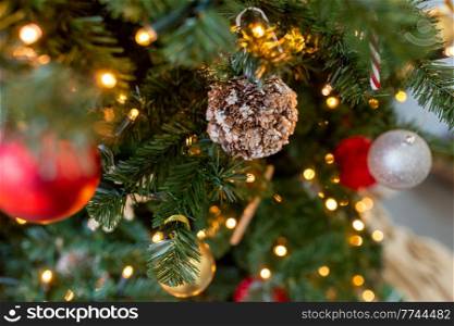 winter holidays, new year and celebration concept - close up of decoration made of cones hanging on artificial christmas tree. decoration made of cones on christmas tree
