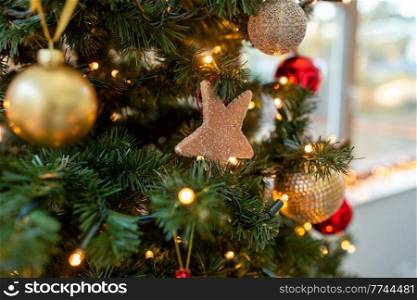 winter holidays, new year and celebration concept - close up of gingerbread star decoration hanging on artificial christmas tree. gingerbread star decoration on christmas tree