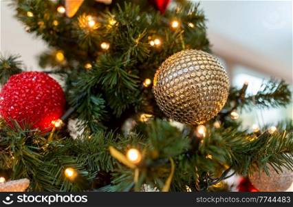 winter holidays, new year and celebration concept - close up of golden christmas ball decoration hanging on artificial fir tree. close up of golden ball on christmas tree