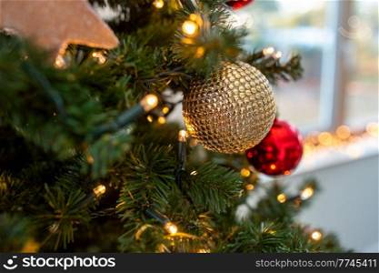 winter holidays, new year and celebration concept - close up of golden christmas ball decoration hanging on artificial fir tree. close up of golden ball on christmas tree