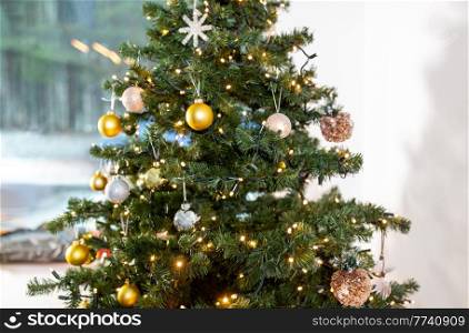 winter holidays, new year and celebration concept - close up of green artificial christmas tree decorated with toys at home. close up of decorated christmas tree at home