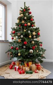 winter holidays, new year and celebration concept - gifts under decorated green artificial christmas tree at home. gifts under decorated christmas tree at home