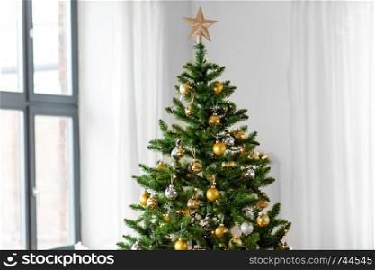 winter holidays, new year and celebration concept - green artificial christmas tree decorated with toys at home. decorated artificial christmas tree at home
