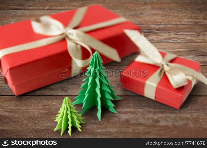 winter holidays, new year and celebration concept - red gift boxes and origami christmas trees on wooden boards background. gift boxes and christmas trees on wooden boards