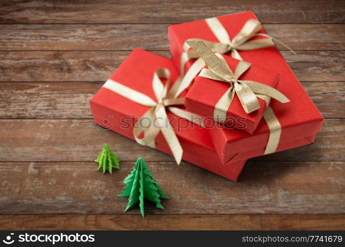 winter holidays, new year and celebration concept - red gift boxes and origami christmas trees on wooden boards background. gift boxes and christmas trees on wooden boards