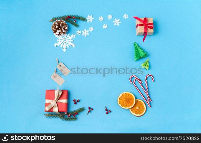 winter holidays, new year and christmas concept - frame made of gift boxes, fir tree branches, tags and decorations on blue background. frame of gifts, fir branches, tags and decorations