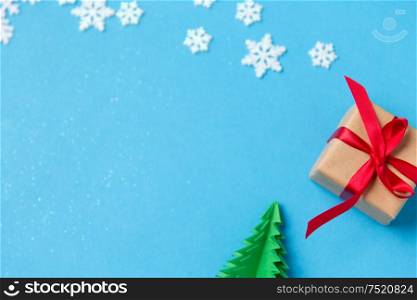 winter holidays, new year and christmas concept - gift box with red bow, christmas tree origami and snowflakes decorations on blue background. gift box, christmas tree origami and snowflakes