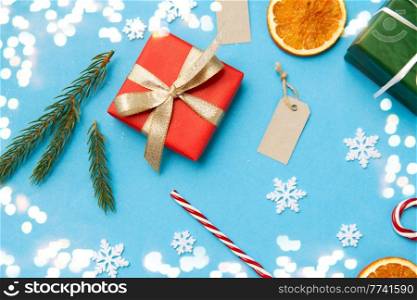 winter holidays, new year and christmas concept - gift boxes, fir tree branches, tags and decorations on blue background with bokeh lights. christmas gifts, branches, tags and decorations