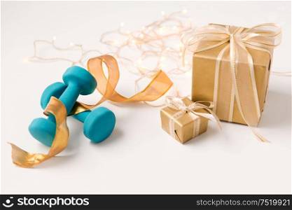 winter holidays, new year and christmas concept - gift boxes wrapped into golden paper and blue dumbbells on white background. christmas gift boxes and dumbbells on white