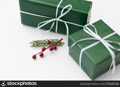 winter holidays, new year and christmas concept - gift boxes wrapped into green paper and fir tree branch with red berries on white background. green gift boxes and fir tree branch with berries