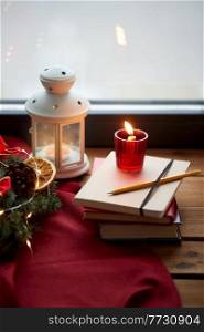 winter holidays, new year and decorations concept - christmas fir wreath, books, candle and lantern on window sill at home. christmas wreath, books, candle, lantern on window