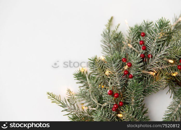 winter holidays, new year and decorations concept - wreath of fir branches with red berries and garland lights on white background. christmas fir wreath with berries and lights