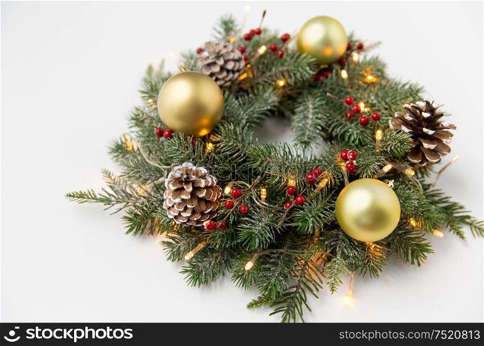 winter holidays, new year and decorations concept - wreath of fir branches with golden balls, pine cones and garland lights on white background. christmas fir wreath with balls, cones and lights