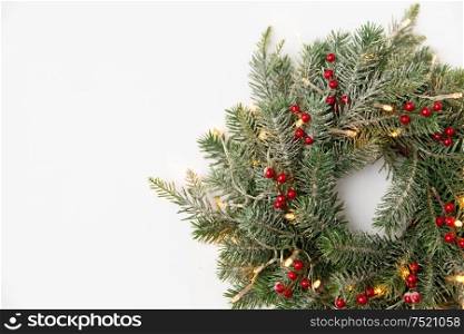 winter holidays, new year and decorations concept - wreath of fir branches with red berries and garland lights on white background. christmas fir wreath with berries and lights