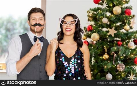 winter holidays, people and celebration concept - happy couple posing with party props over christmas tree lights background. happy couple with party props on christmas