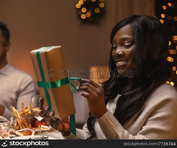 winter holidays, people and celebration concept - happy woman opening christmas presents at dinner party. woman opening christmas present at dinner party