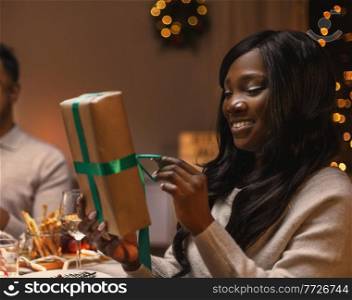 winter holidays, people and celebration concept - happy woman opening christmas presents at dinner party. woman opening christmas present at dinner party