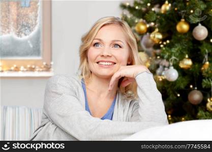 winter holidays, people and leisure concept - happy middle aged woman at home over christmas tree lights on background. portrait of happy woman at home on christmas