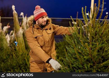 winter holidays, sale and people concept - happy smiling man buying christmas tree at street market in evening. happy man buying christmas tree at market