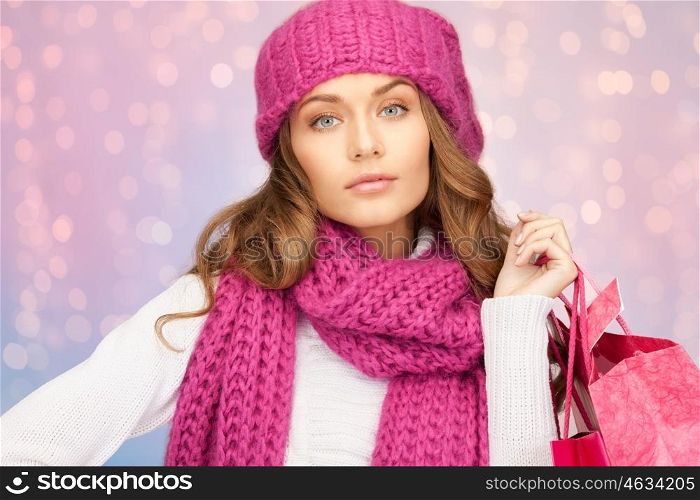 winter holidays, sale, christmas and people concept - beautiful young woman in hat and mittens with shopping bags over rose quartz and serenity lights background