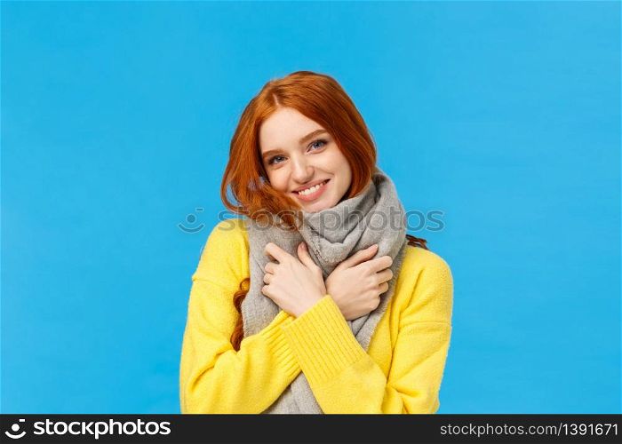 Winter holidays, sales and shopping concept. Waist-up portrait cute and lovely redhead woman wrap neck with soft warm scarf, tilt head smiling happily, embrace herself, standing blue background.. Winter holidays, sales and shopping concept. Waist-up portrait cute and lovely redhead woman wrap neck with soft warm scarf, tilt head smiling happily, embrace herself, standing blue background