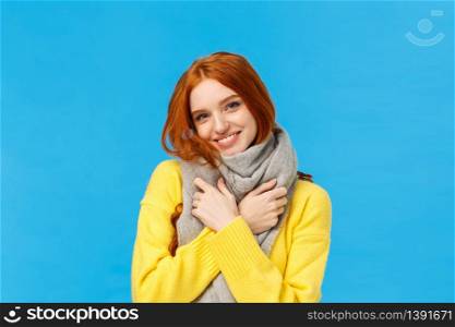Winter holidays, sales and shopping concept. Waist-up portrait cute and lovely redhead woman wrap neck with soft warm scarf, tilt head smiling happily, embrace herself, standing blue background.. Winter holidays, sales and shopping concept. Waist-up portrait cute and lovely redhead woman wrap neck with soft warm scarf, tilt head smiling happily, embrace herself, standing blue background