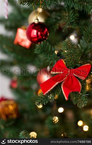 winter holidays, season and luxury concept - close up of red decorations on artificial christmas tree. close up of decorations on christmas tree