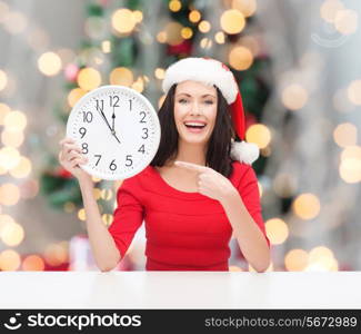 winter, holidays, time and people concept - smiling woman in santa helper hat and red dress with clock over christmas tree and ligths background