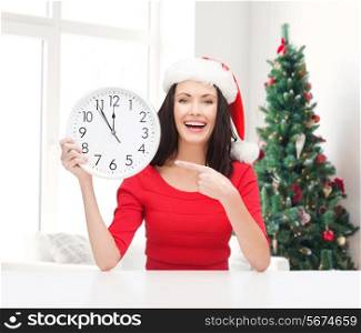winter, holidays, time and people concept - smiling woman in santa helper hat and red dress with clock over living room and christmas tree background