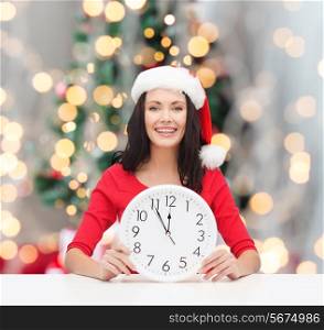 winter, holidays, time and people concept - smiling woman in santa helper hat and red dress with clock over christmas tree lights background