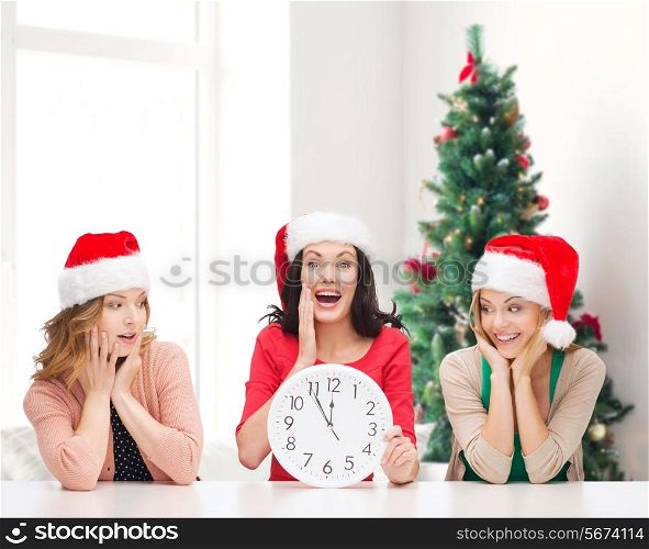 winter, holidays, time and people concept - smiling women in santa helper hats with clock over living room and christmas tree background