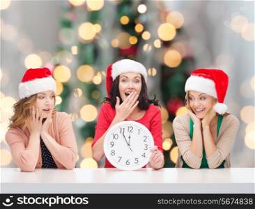 winter, holidays, time and people concept - smiling women in santa helper hats with clock over christmas tree background