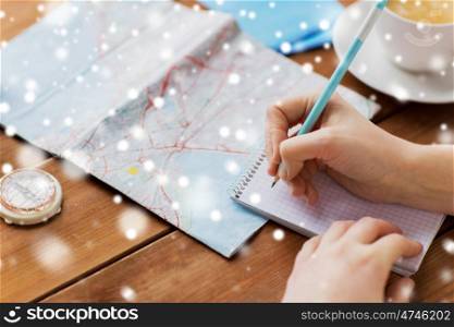 winter holidays, tourism, travel, destination and people concept - traveler hands with map and compass writing to notebook over snow