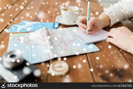 winter holidays, tourism, travel, destination and people concept - traveler hands with map and coffee writing to notebook over snow