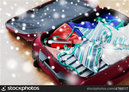 winter holidays, vacation, tourism and objects concept - close up of travel bag with beach clothes and sunscreen over snow