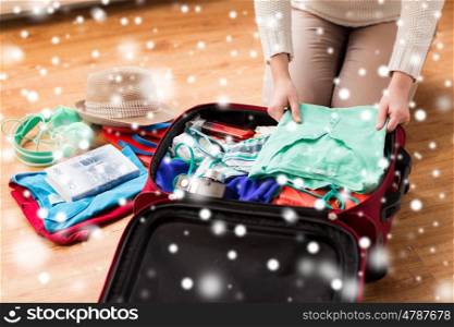 winter holidays, vacation, tourism and objects concept - close up of woman packing travel bag with summer clothes, camera and city guide over snow